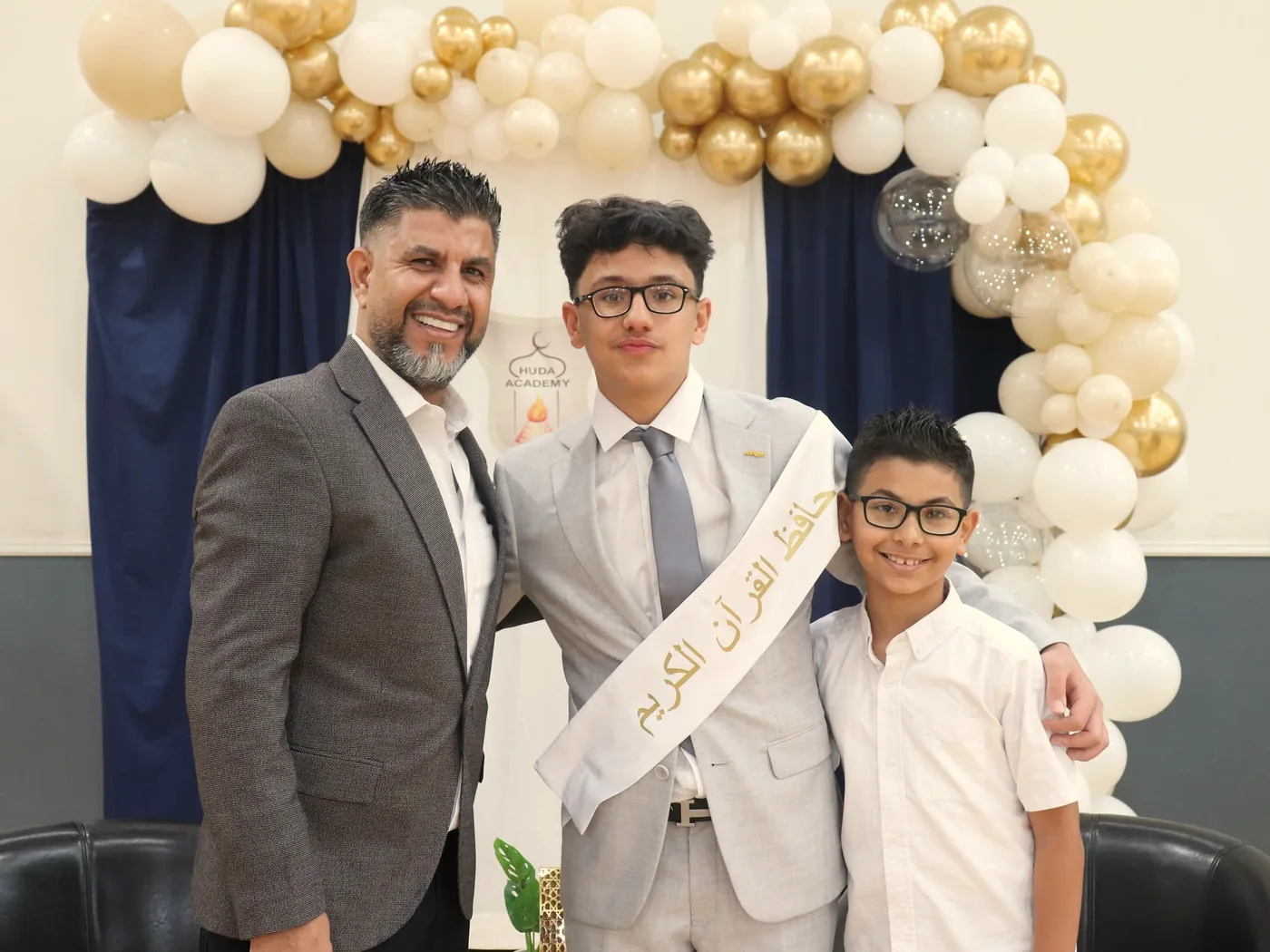 A student wearing a Qur&rsquo;an-memorisation sash at the hifz ceremony, with two others